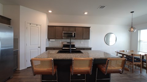 A kitchen with a granite countertop and wooden chairs.