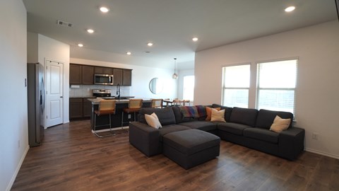 A living room with a black couch and a kitchen area in the background.