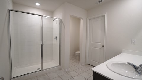 A white bathroom with a walk-in shower and a toilet in the background.