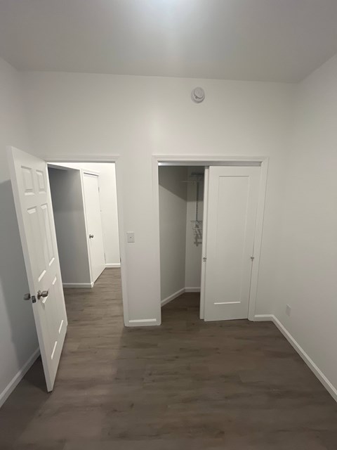 A room with white walls and a wooden floor with two open doors.