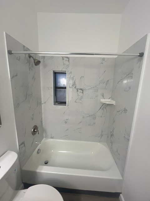 A white bathroom with a marble wall and a white tub.
