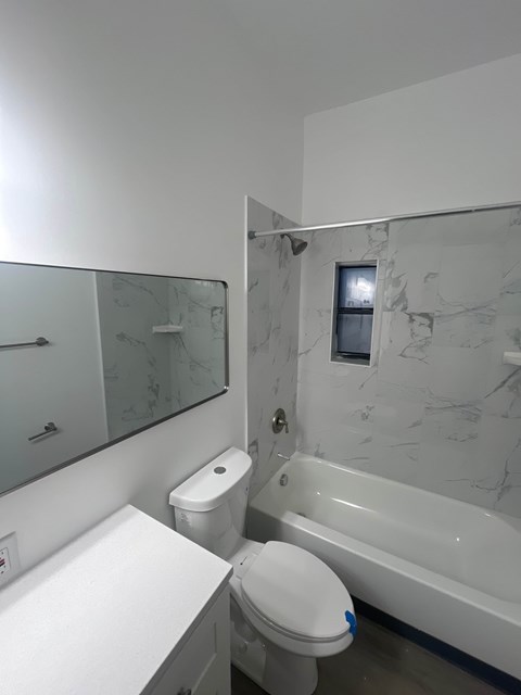 A white toilet with a blue sticker on the lid is in a bathroom with a marble wall and a glass shower door.