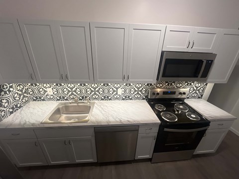 A kitchen with white cabinets and a black and white tiled backsplash.