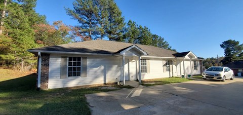 A white house with a grey roof and a car parked in front.
