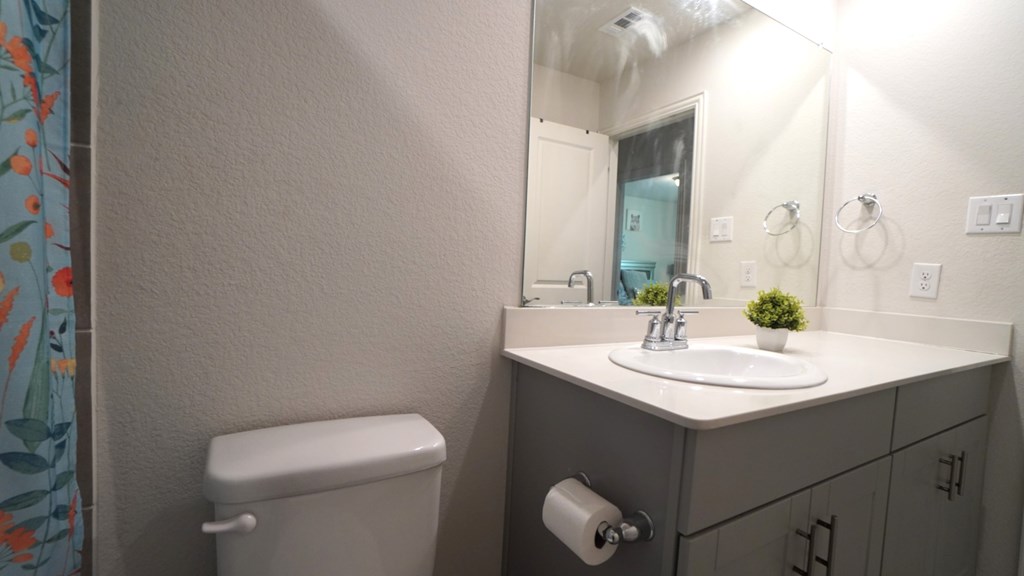 A bathroom with a toilet, sink, and mirror.