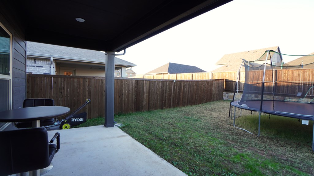 A trampoline is on the grass in a backyard.