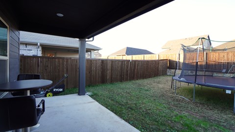 A trampoline is on the grass in a backyard.