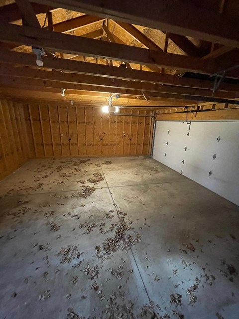 A room with wooden walls and ceiling, and a concrete floor with debris scattered across it.