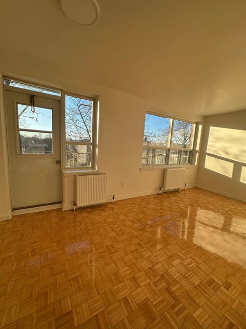 A room with wooden flooring and a view of a tree through the window.