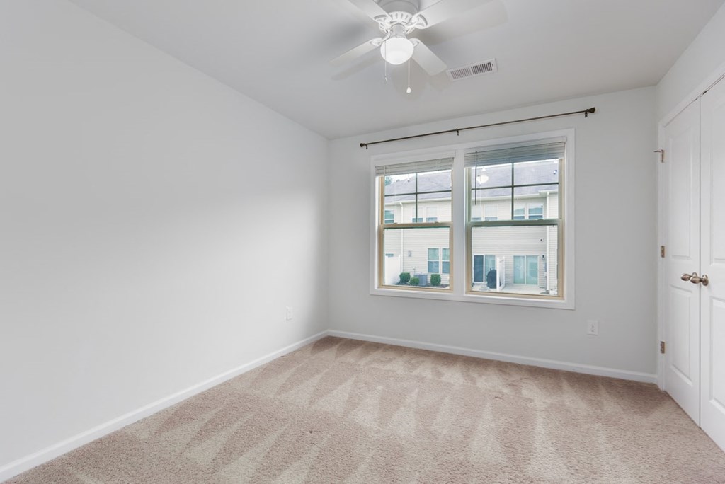 A room with a carpeted floor and a ceiling fan.