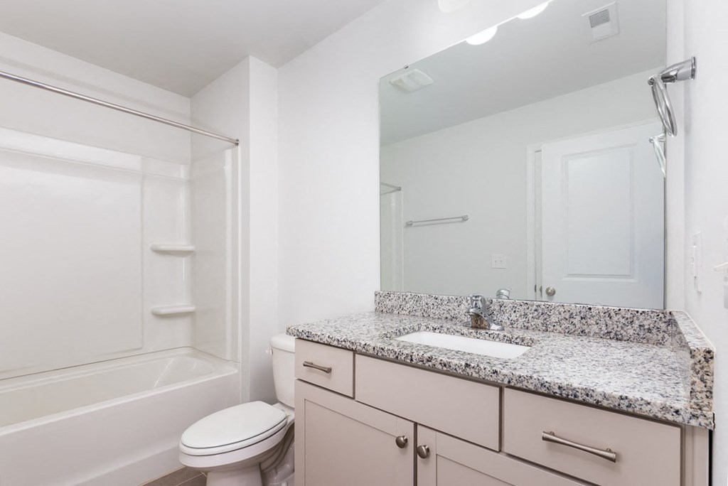 A white bathroom with a granite counter top and a toilet.