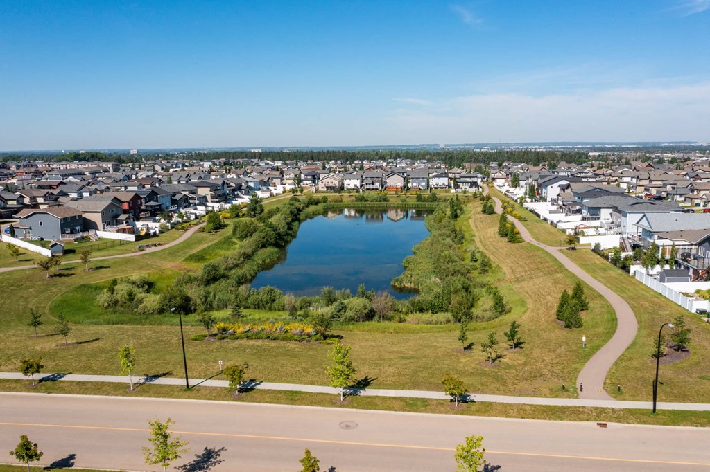 A small lake in the middle of a park with houses in the background.