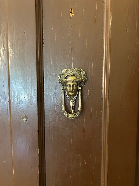 A brass door knocker shaped like a woman's head is on a wooden door.