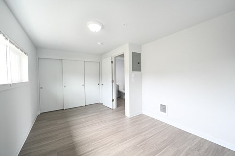 A room with white walls and wooden flooring with a doorway leading to another room.