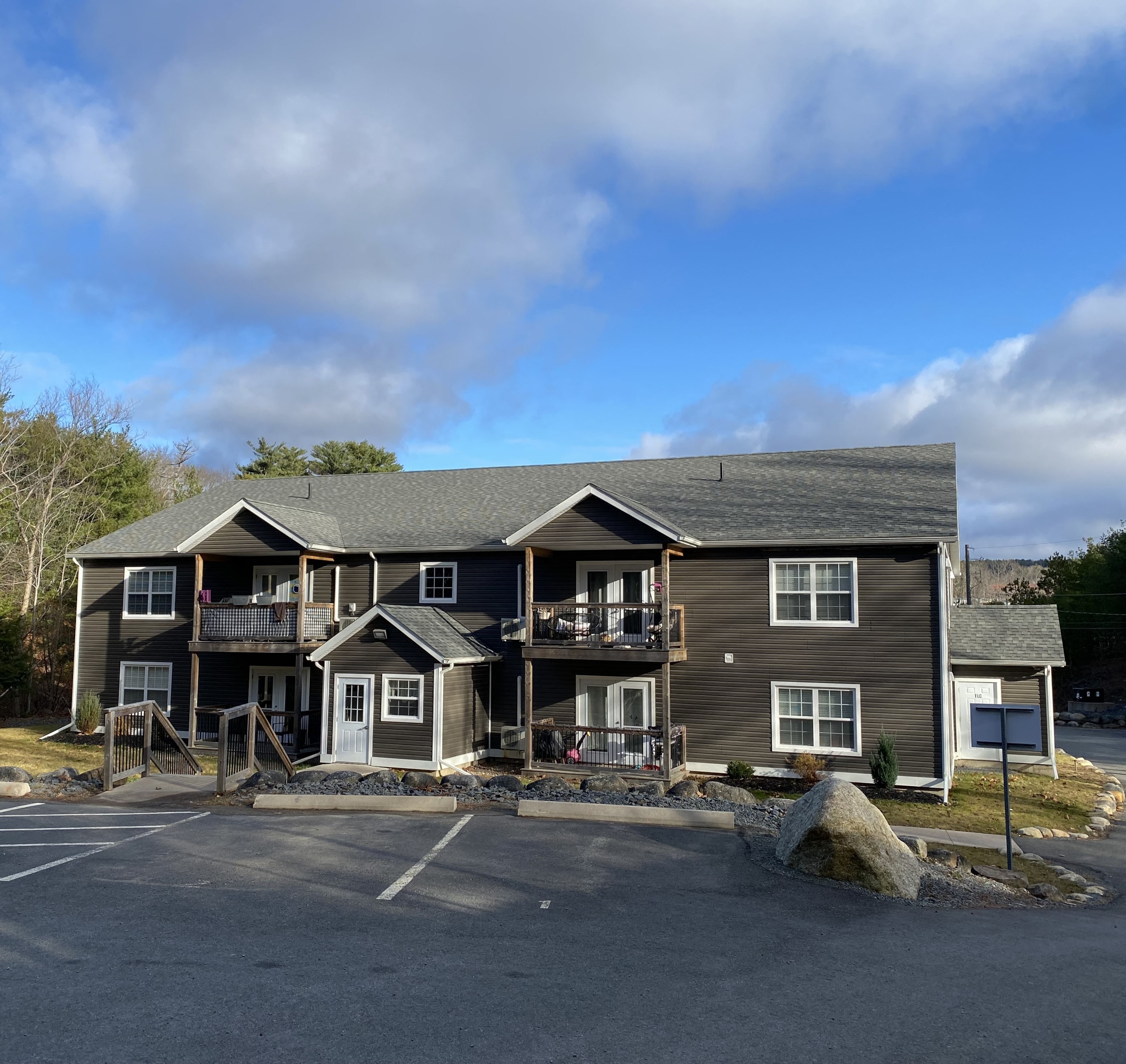 A large two-story building with a grey roof and a parking lot in front.