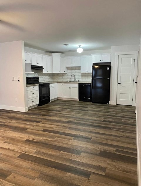 A kitchen with black appliances and wooden floors.