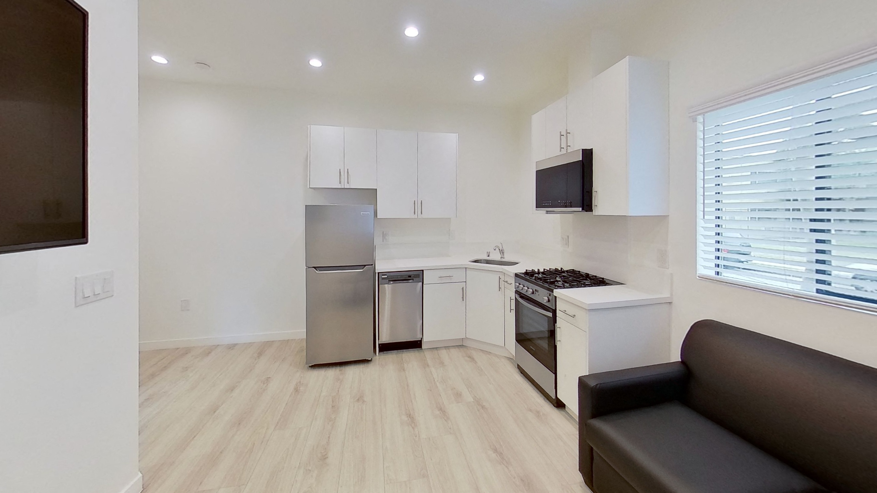 A modern kitchen with a stainless steel refrigerator and a black couch.
