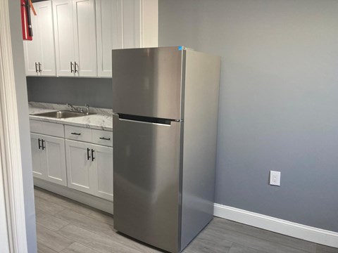 A stainless steel refrigerator stands in a kitchen with white cabinets.