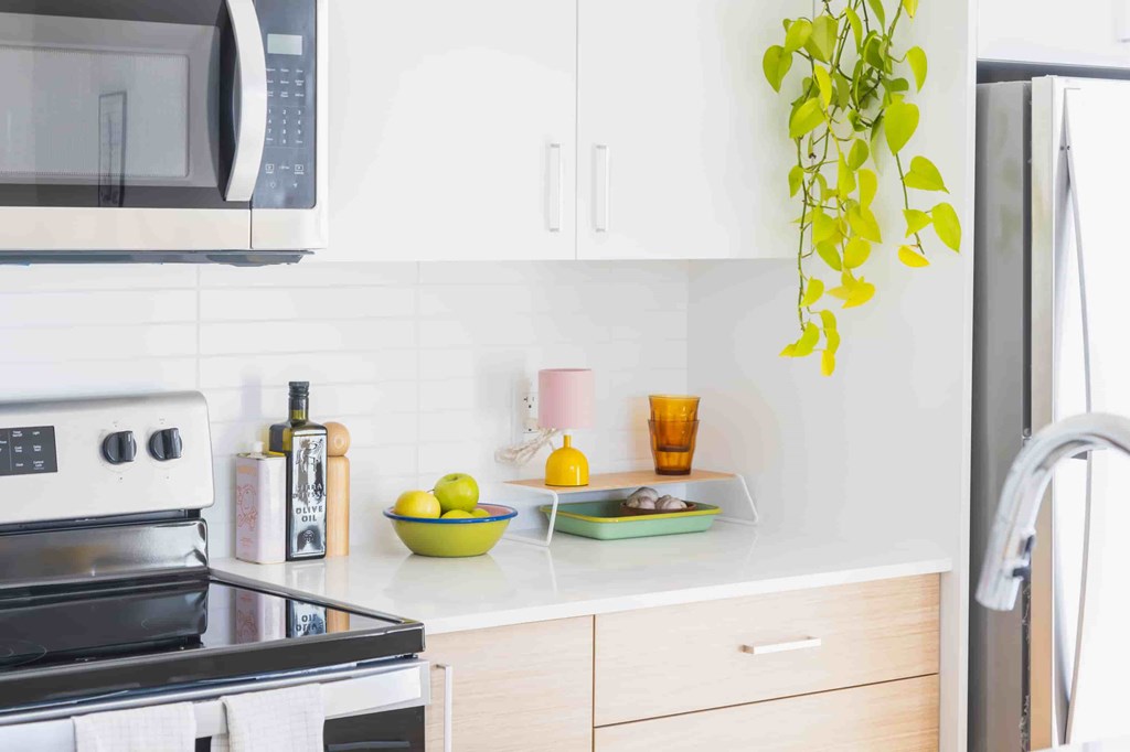 A kitchen with a black stove top oven, a microwave, a plant, and a bowl of fruit on the counter.