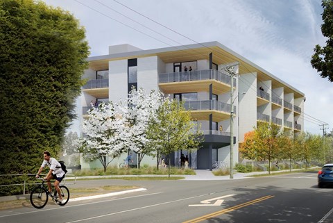 A man rides his bike past a modern apartment building.