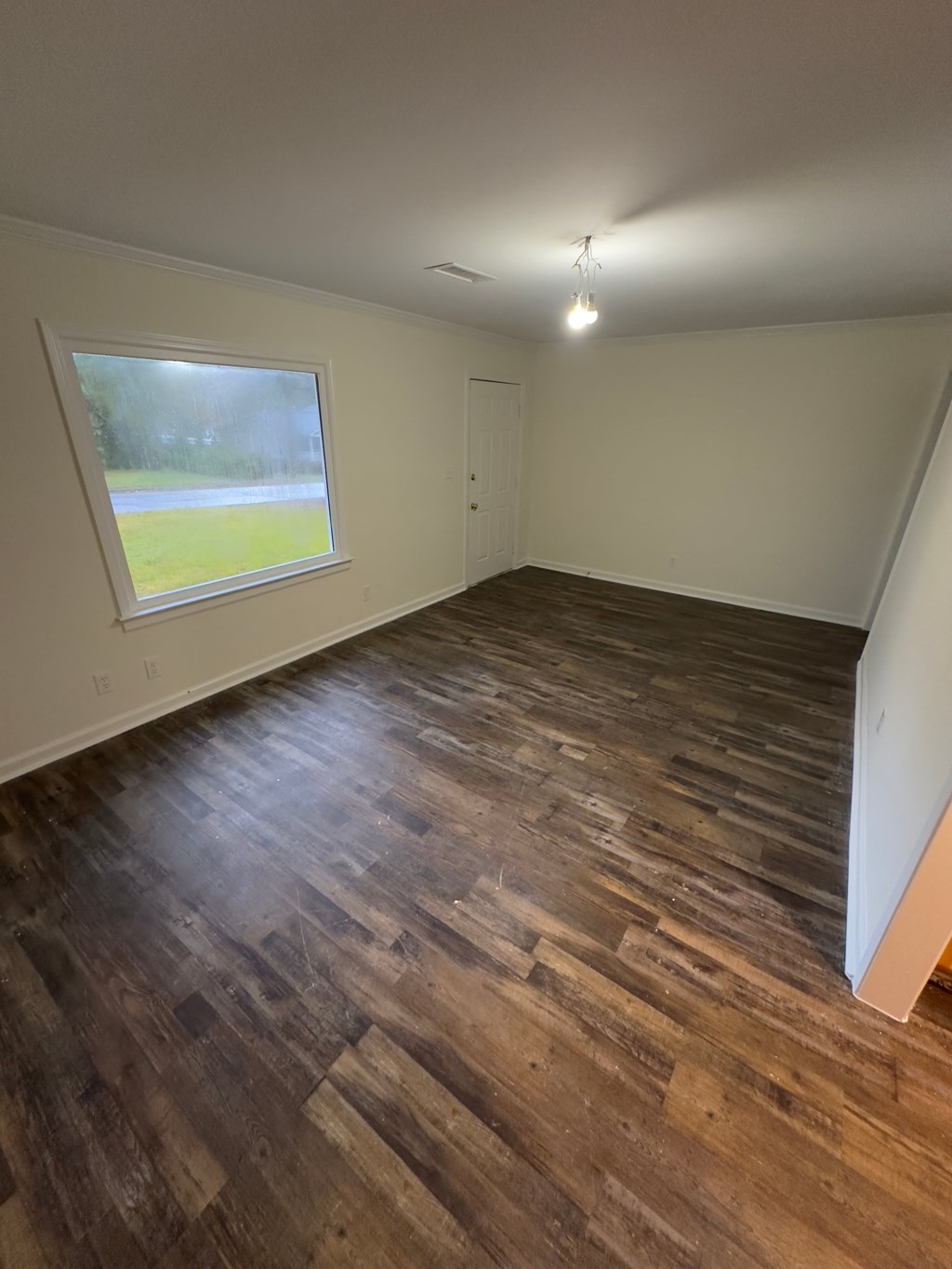 A room with wooden flooring and a window overlooking a grassy area.