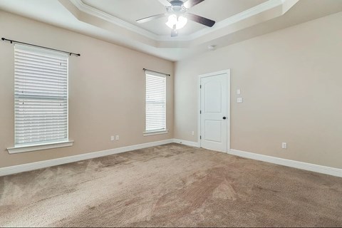 A room with a carpeted floor, a ceiling fan, and a window with blinds.