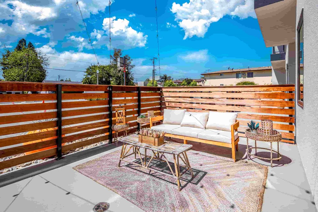 A patio with a white couch, wooden table, and a woven basket on a colorful rug.