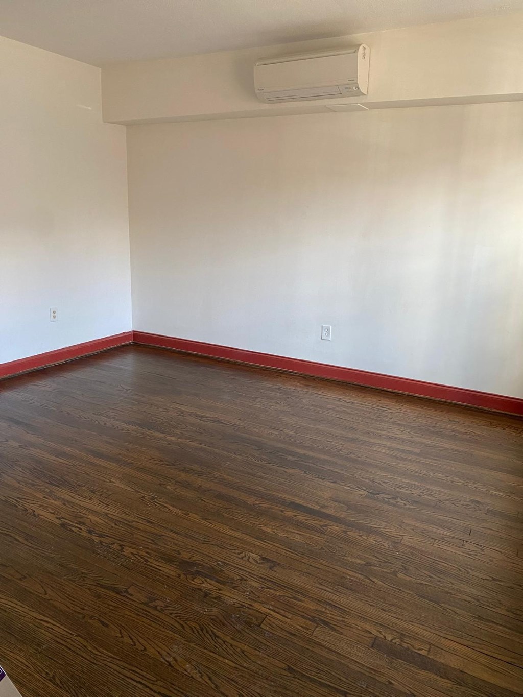 A room with a wooden floor and a red stripe along the bottom.