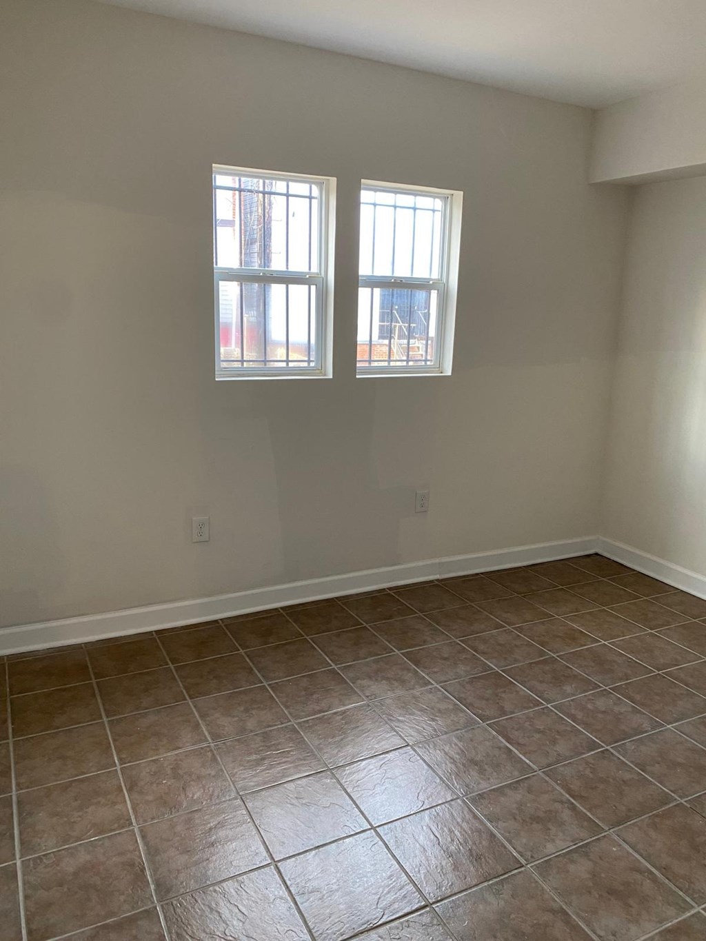 A room with tile flooring and two windows.