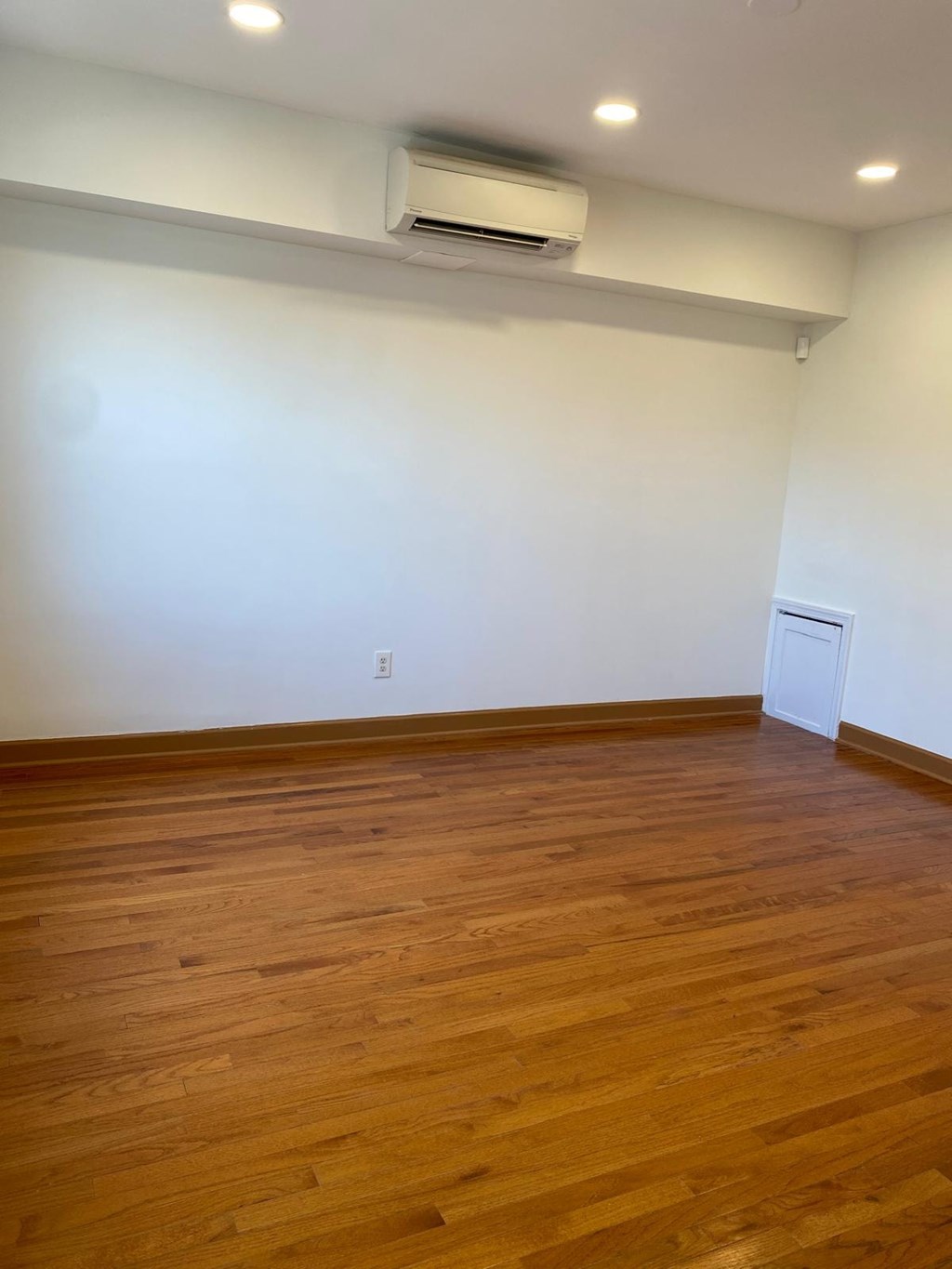 A room with wooden flooring and a white wall with a door on the right side.