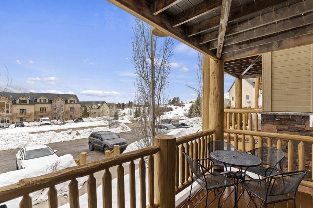A wooden deck with a table and chairs overlooking a snowy street.