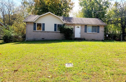 A small house with a white door and a small window is surrounded by a grassy area.