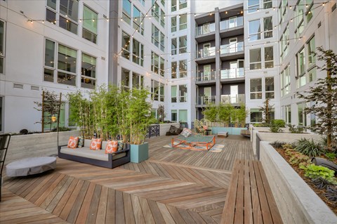 A wooden deck with a bench and plants in the foreground and apartment buildings in the background.