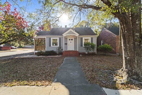 A house with a grey roof and a red door is surrounded by trees and leaves.