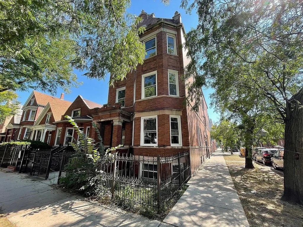A tall brick building with a tower sits on a tree-lined street.