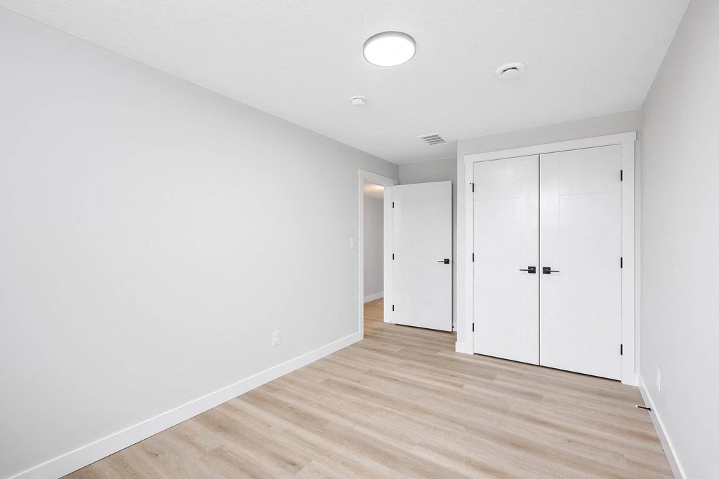 A white room with a wooden floor and three white doors.