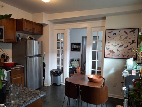 A kitchen with a refrigerator, a table and chairs, and a painting on the wall.