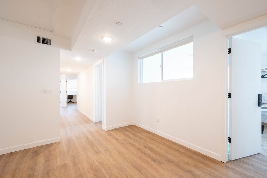 A room with white walls and wooden flooring with a window on the right wall.