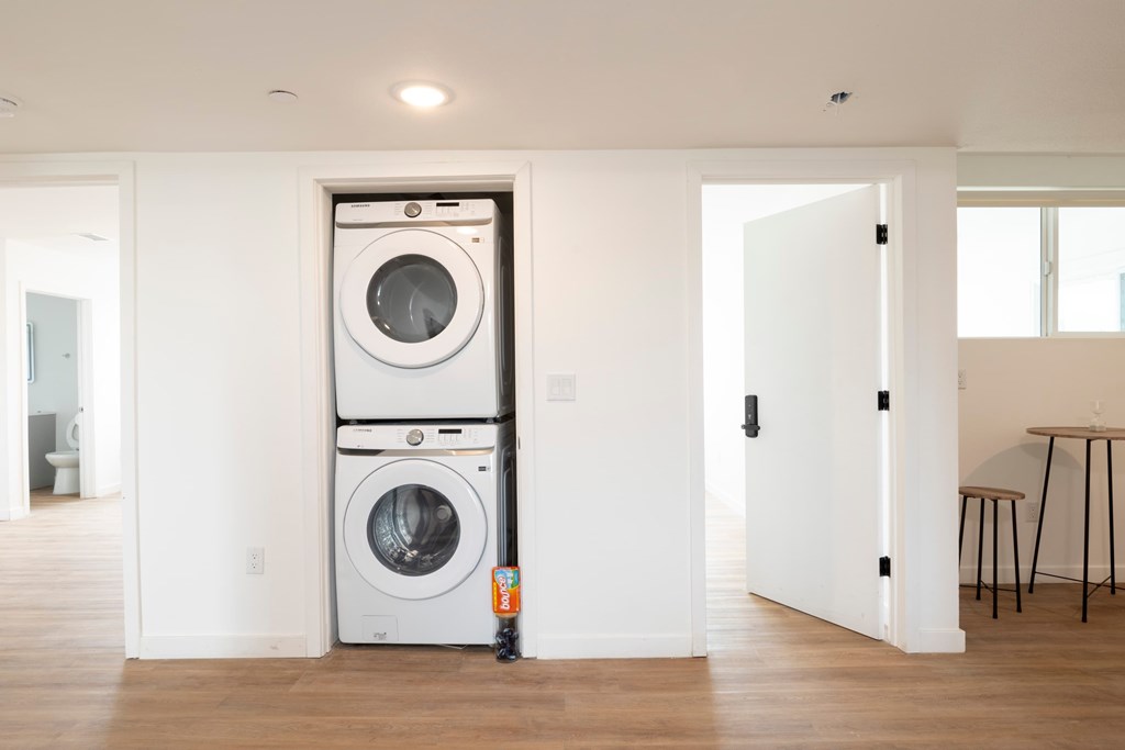 A white door is open to a room with a washer and dryer stacked on top of each other.