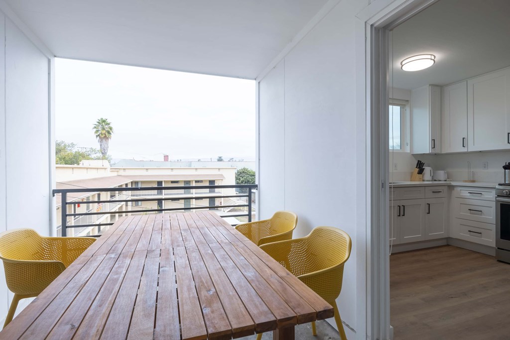 A dining table with yellow chairs is in a room with a view of a balcony.