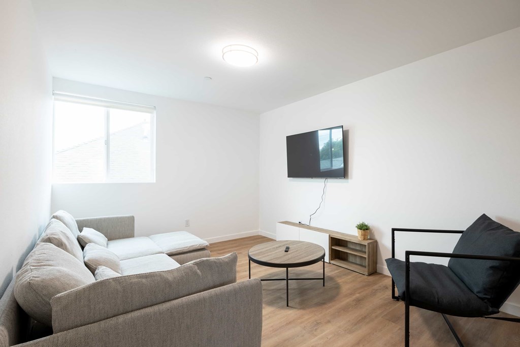 A living room with a grey couch, a black chair, and a flat screen TV mounted on the wall.