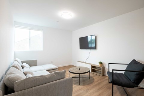 A living room with a grey couch, a black chair, and a flat screen TV mounted on the wall.
