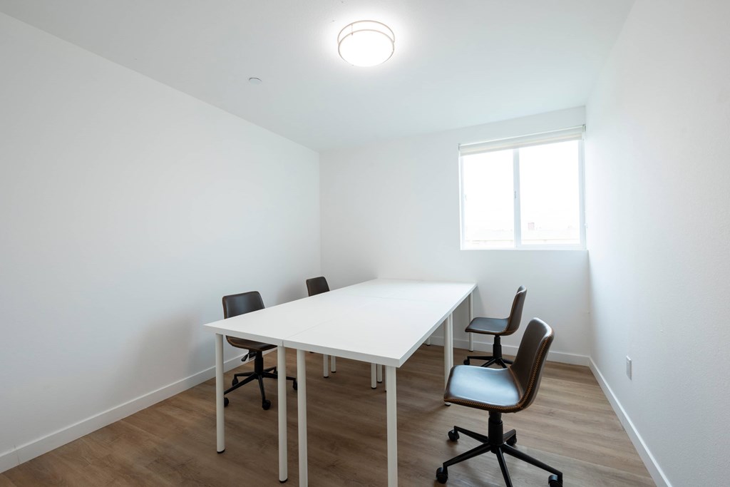 A white table with four chairs is in a room with a window.