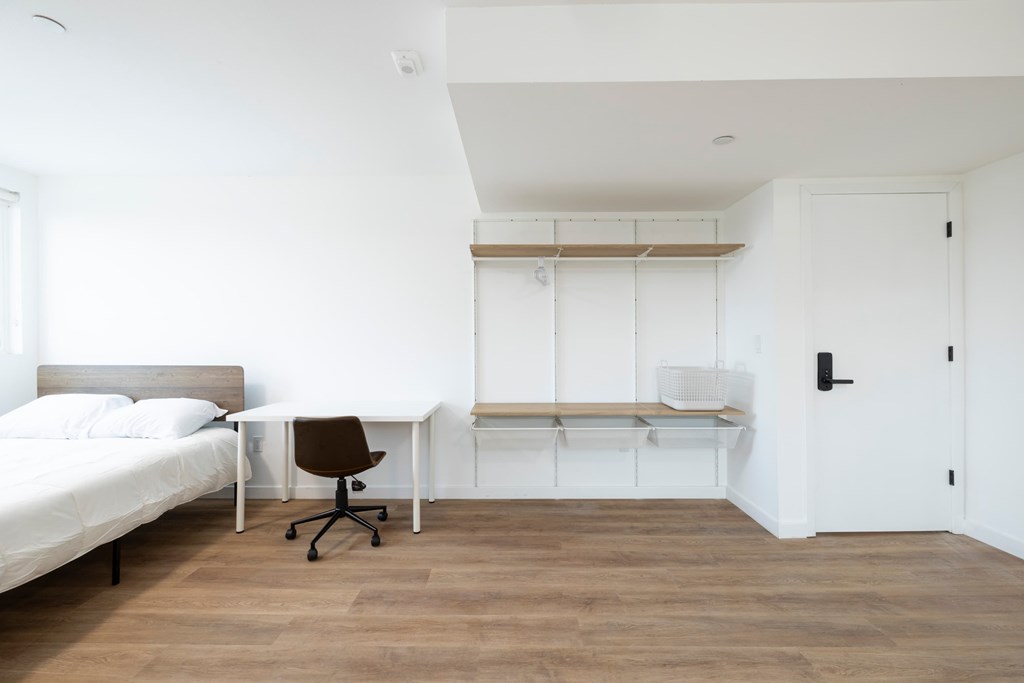 A white bedroom with a bed, desk, and chair.