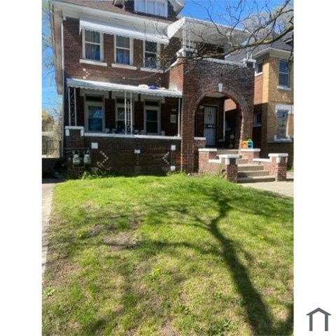 A house with a large front yard and a tree casting a shadow on the grass.