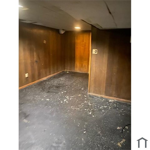 A room with a wooden door and a grey floor with some debris scattered around.