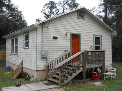 A small house with a red door and a wooden staircase leading to the door.