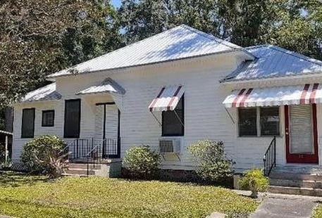 A white house with a red door and striped awnings.