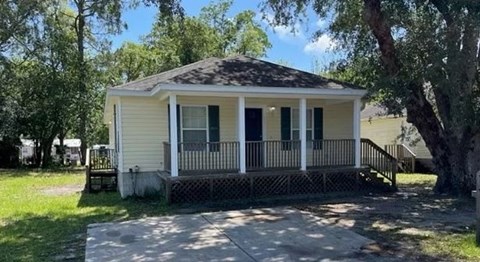 A small white house with a porch and a tree in front.