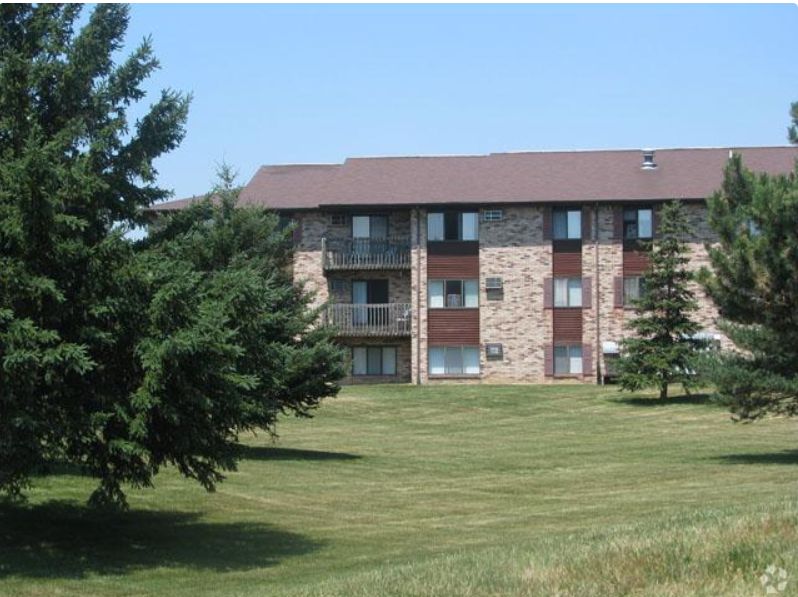 A large building with a balcony is surrounded by trees.